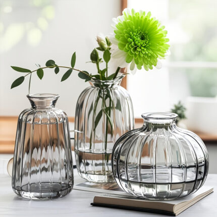 Three vertical striped transparent glass vases in different shapes displayed on indoor table, used for fresh flower arrangement and modern home desktop decorative display