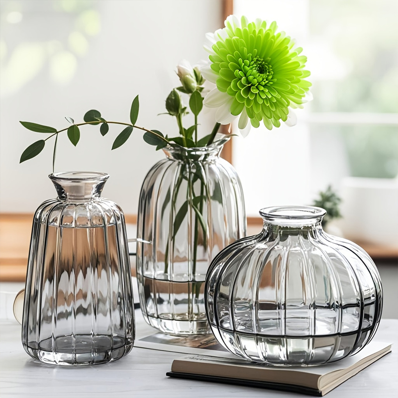 Three vertical striped transparent glass vases in different shapes displayed on indoor table, used for fresh flower arrangement and modern home desktop decorative display