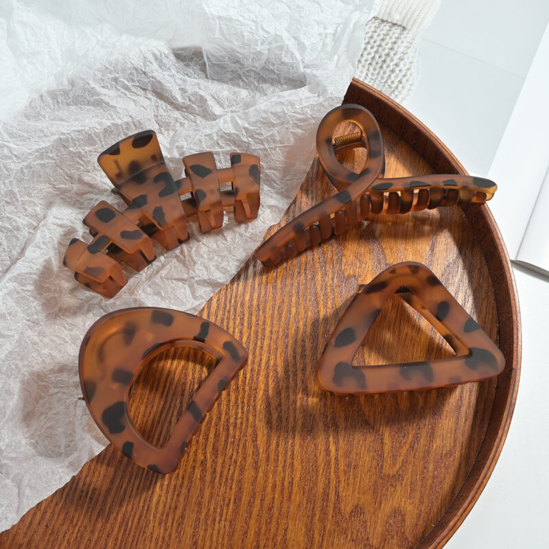 Four matte tortoise leopard print large shark hair claw clips with mixed hollow shapes on wooden tray