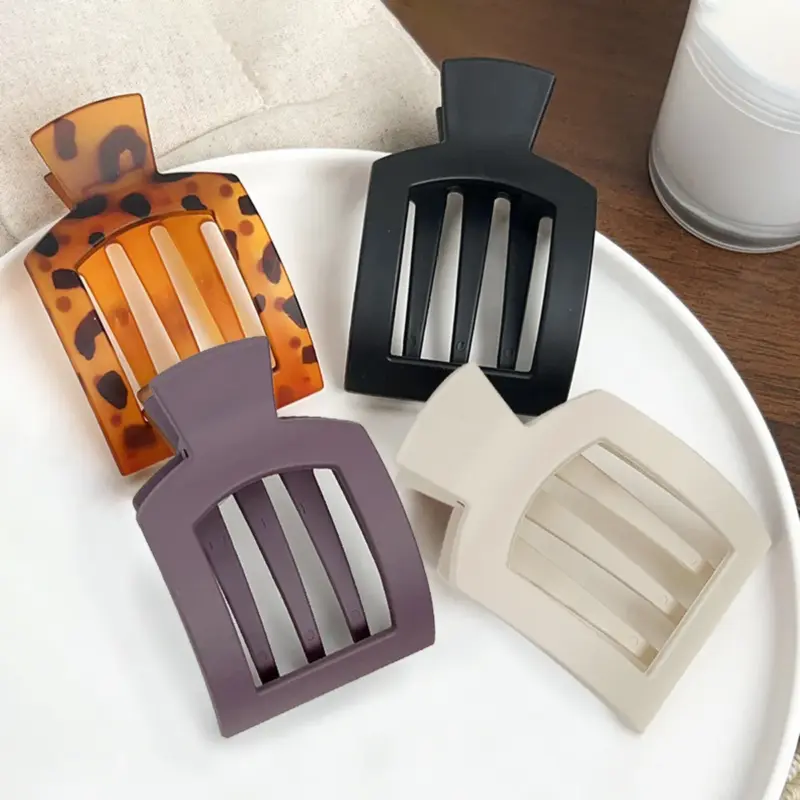 Four matte hollow square large duckbill hair clips in tortoiseshell, black, purple and off-white arranged on white plate