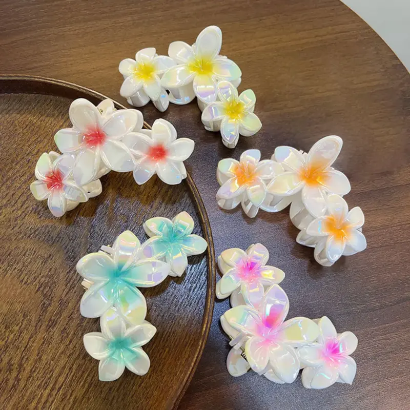 Multicolor iridescent electroplated plumeria flower hair claw clips set displayed on wooden table