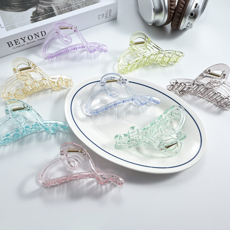 Multicolor transparent hollow heart plastic hair claw clips arranged on white table and ceramic plate for women hairstyling