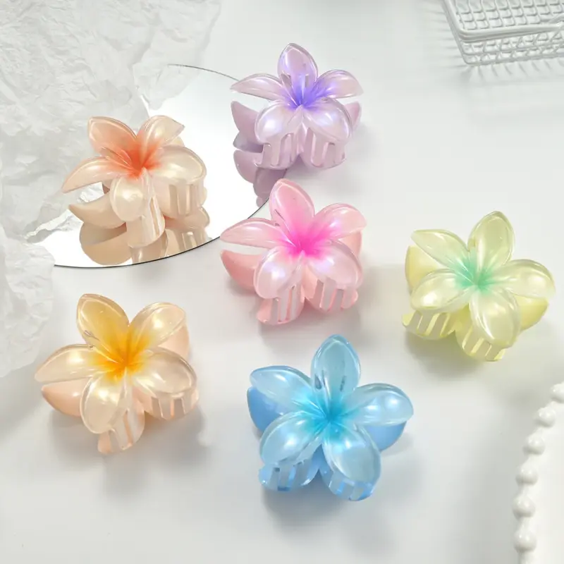 Six gradient iridescent translucent plumeria flower hair claw clips in assorted pastel colors arranged on white table
