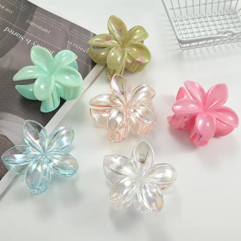 Six translucent iridescent plumeria flower shark hair claw clips in assorted pastel shades on white table