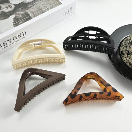 Four matte frosted hollow triangle and semicircle shark hair claw clips in solid & tortoise colors on white table