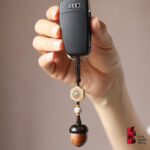 Hand holding a car key fitted with retro handmade wooden acorn keychain decorated with floral beads, used as delicate decorative pendant for car keys and handbags in daily life