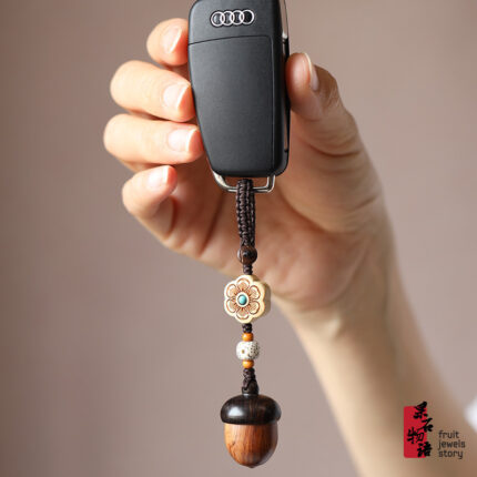 Hand holding a car key fitted with retro handmade wooden acorn keychain decorated with floral beads, used as delicate decorative pendant for car keys and handbags in daily life