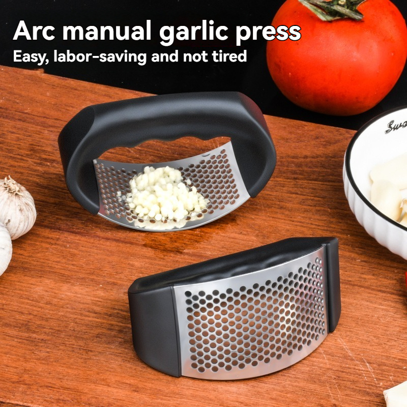 Curved ergonomic stainless steel manual garlic press with black non-slip handle, used to quickly crush garlic and ginger for seasoning preparation in home kitchen cooking.